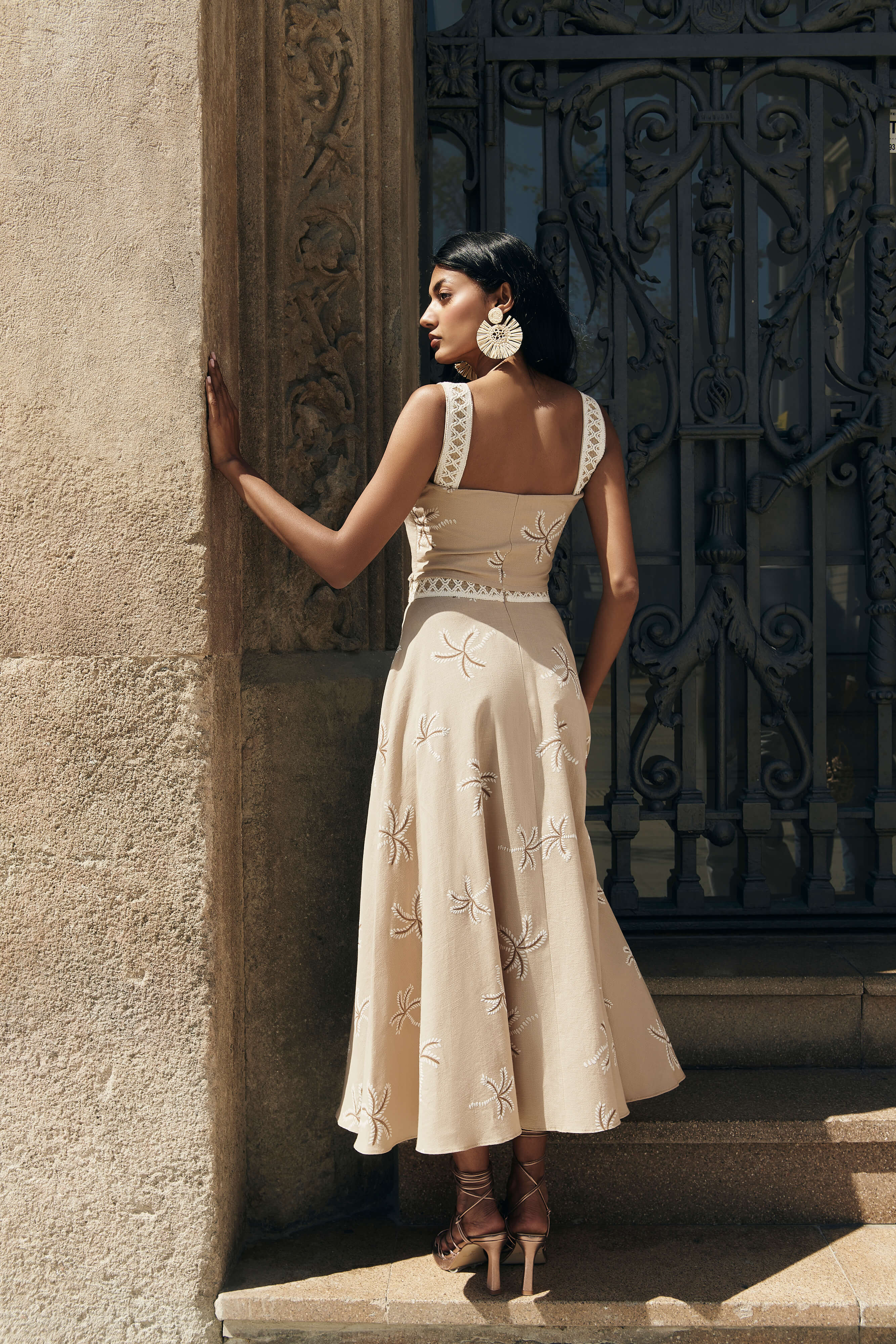 Falda Palmar midi con vuelo y nesgas, estampado de palmeras beige. Cinta decorativa en la cadera y cremallera trasera