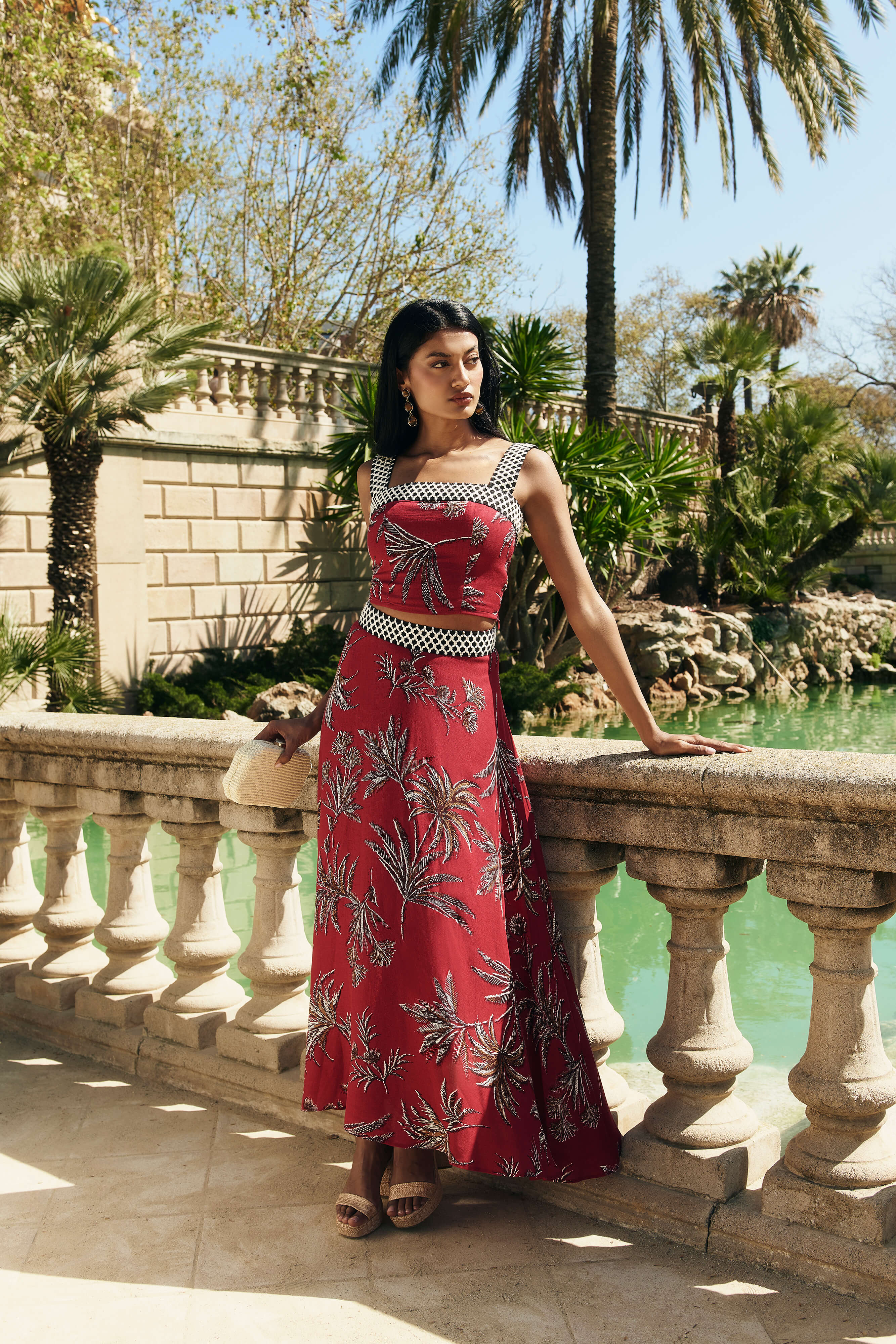 Falda Palmar midi con vuelo y nesgas, estampado de palmeras granate. Cinta decorativa en la cadera y cremallera trasera.