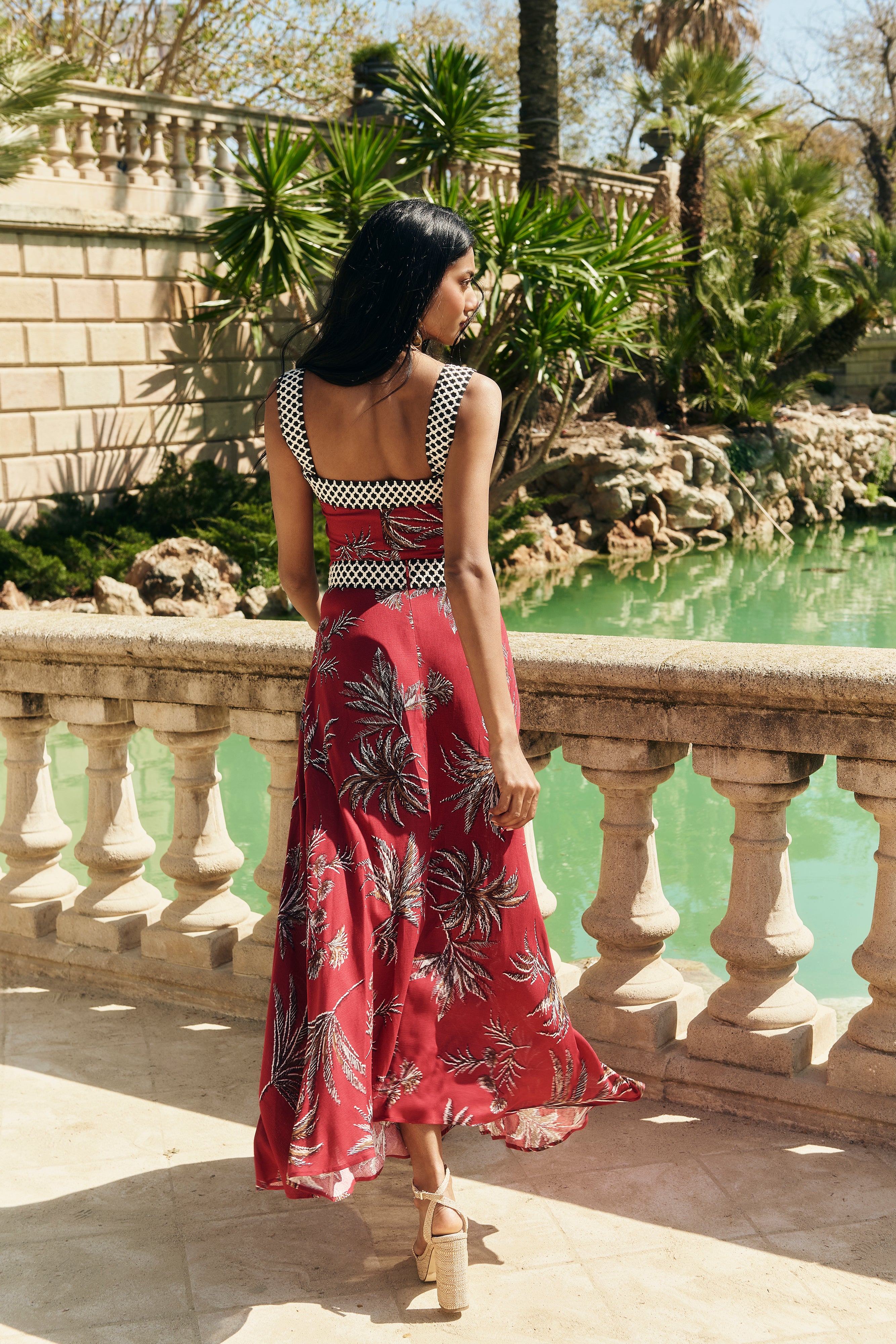 Falda Palmar midi con vuelo y nesgas, estampado de palmeras granate. Cinta decorativa en la cadera y cremallera trasera.