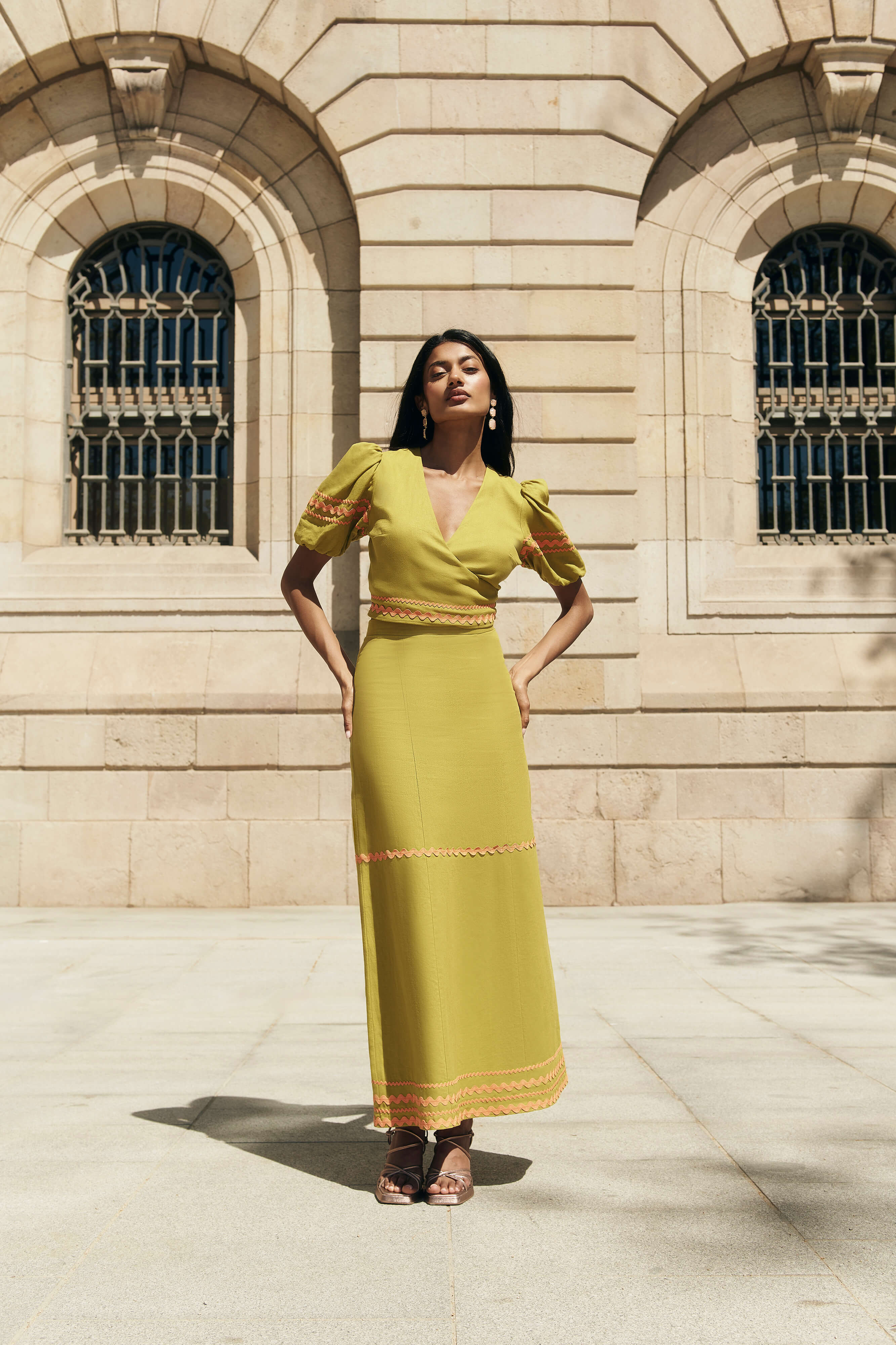 Falda Sabina en Verde oliva de lino y viscosa con corte midi, cintas decorativas naranjas y cremallera trasera.