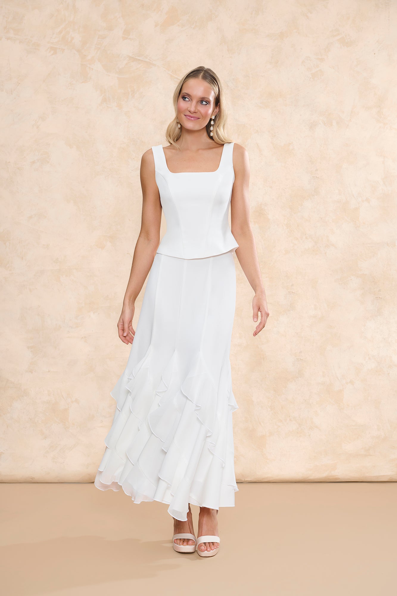 Fotografía de frente del conjunto "Samara" de Miphai en color blanco. El look consta de un top de escote cuadrado con tirantes anchos. Completan el conjunto unas sandalias de plataforma blancas y pendientes largos, sobre un fondo neutro.