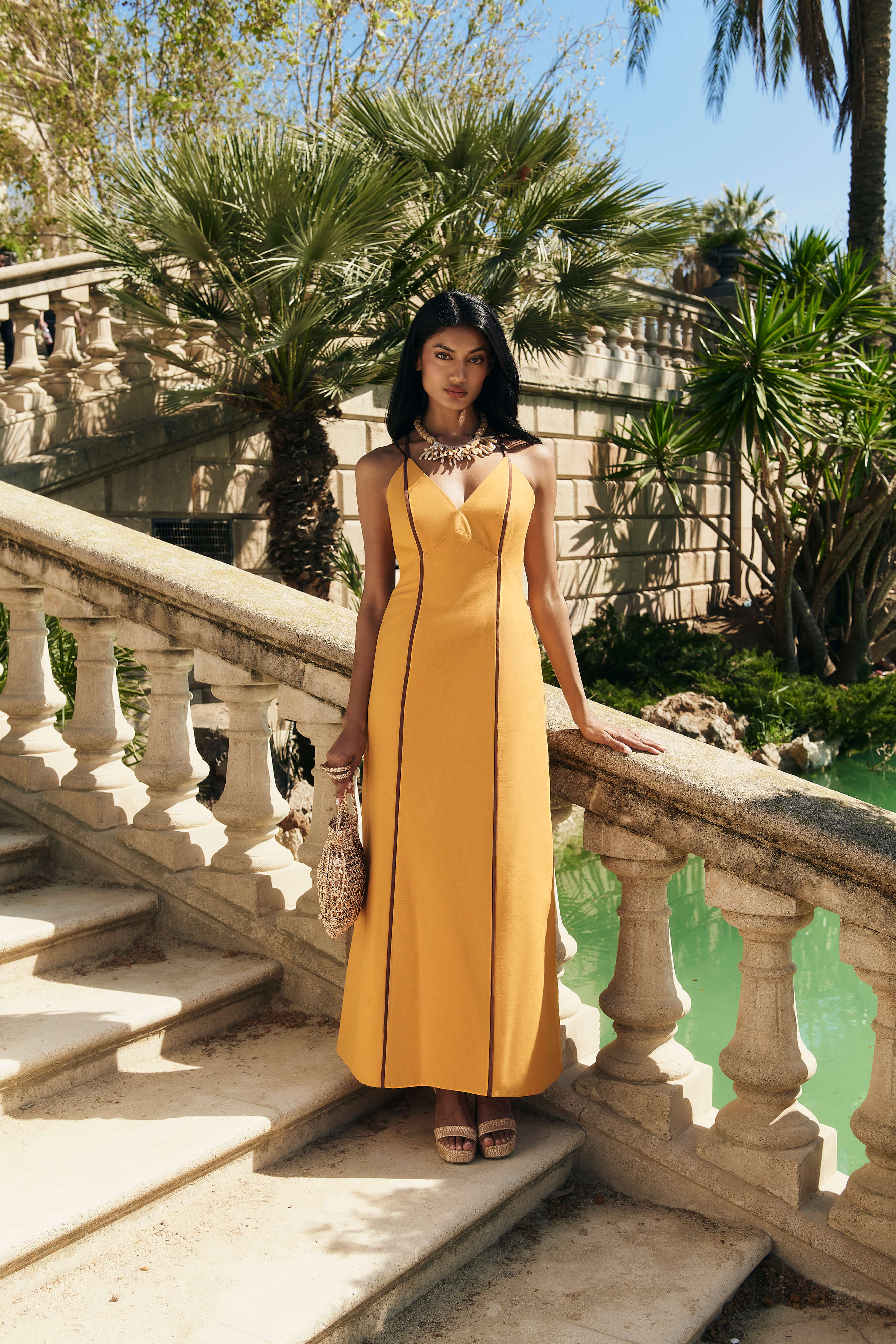 Vestido Capri largo en mostaza con detalles en marrón chocolate, lino fluido, escote en pico, tirantes cruzados y falda con movimiento.