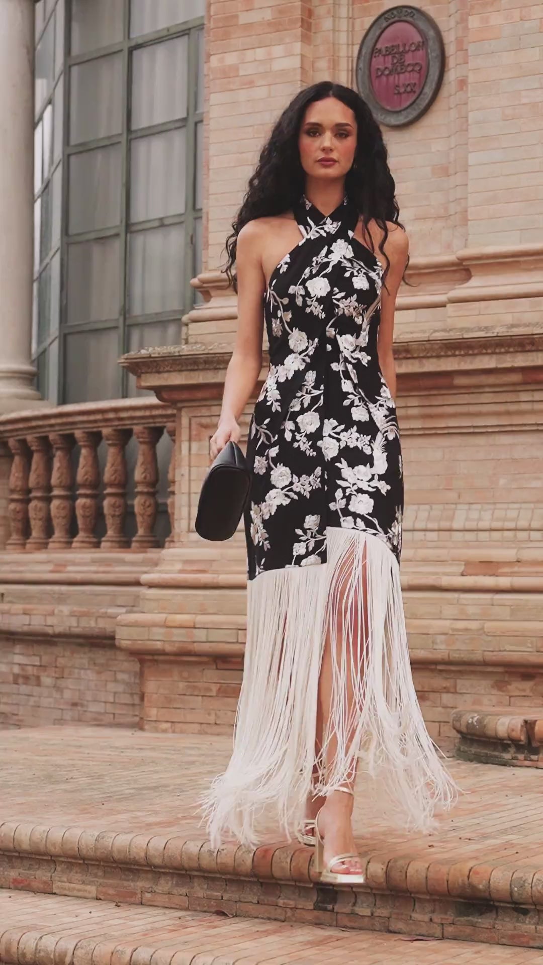 Vestido Candela Midi Negro, confeccionado en viscosa con bordado floral marfil, presenta un cuello halter , corte semi-entallado y falda con flecos