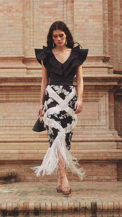 La falda Adela Negro es una falda midi de viscosa con bordado floral marfil y flecos en tres tamaños que forman un diseño en zigzag hasta el bajo.